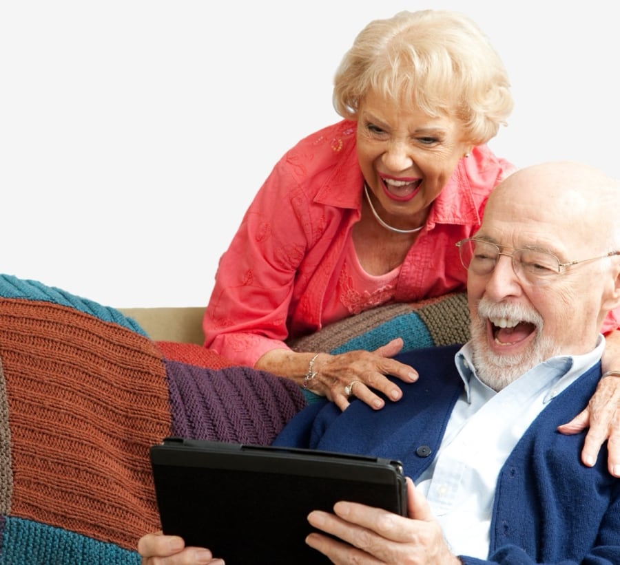 Senior couple laughing over a shared iPad watching the grandchildren home videos